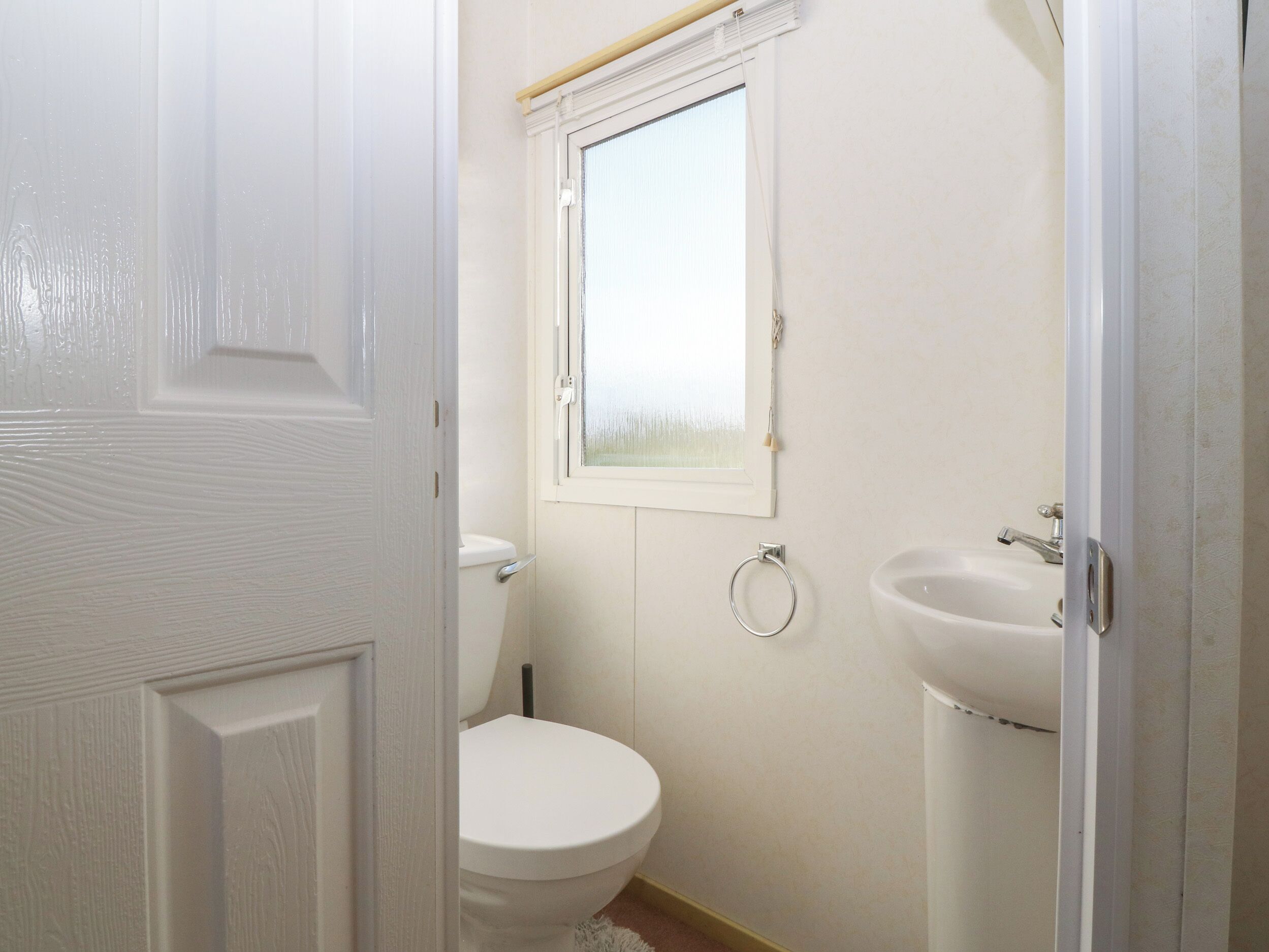 A small, clean bathroom with a toilet, sink, and window.