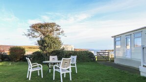 A grassy outdoor area with a table and four chairs, a tree, and a mobile home with a gate. - Tir Glyn Caravan (Pwllheli)