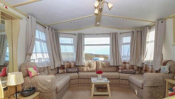 A cozy living room with a sectional sofa, a small coffee table, and a lamp. - Tir Glyn Caravan (Pwllheli)