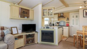 A compact living space with a sofa, television, kitchen area, and dining table. - Tir Glyn Caravan (Pwllheli)