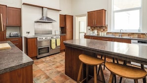 Une cuisine moderne avec des meubles en bois, une hotte en acier inoxydable, un four encastré, un grand îlot central avec des tabourets et une fenêtre qui laisse entrer la lumière naturelle.