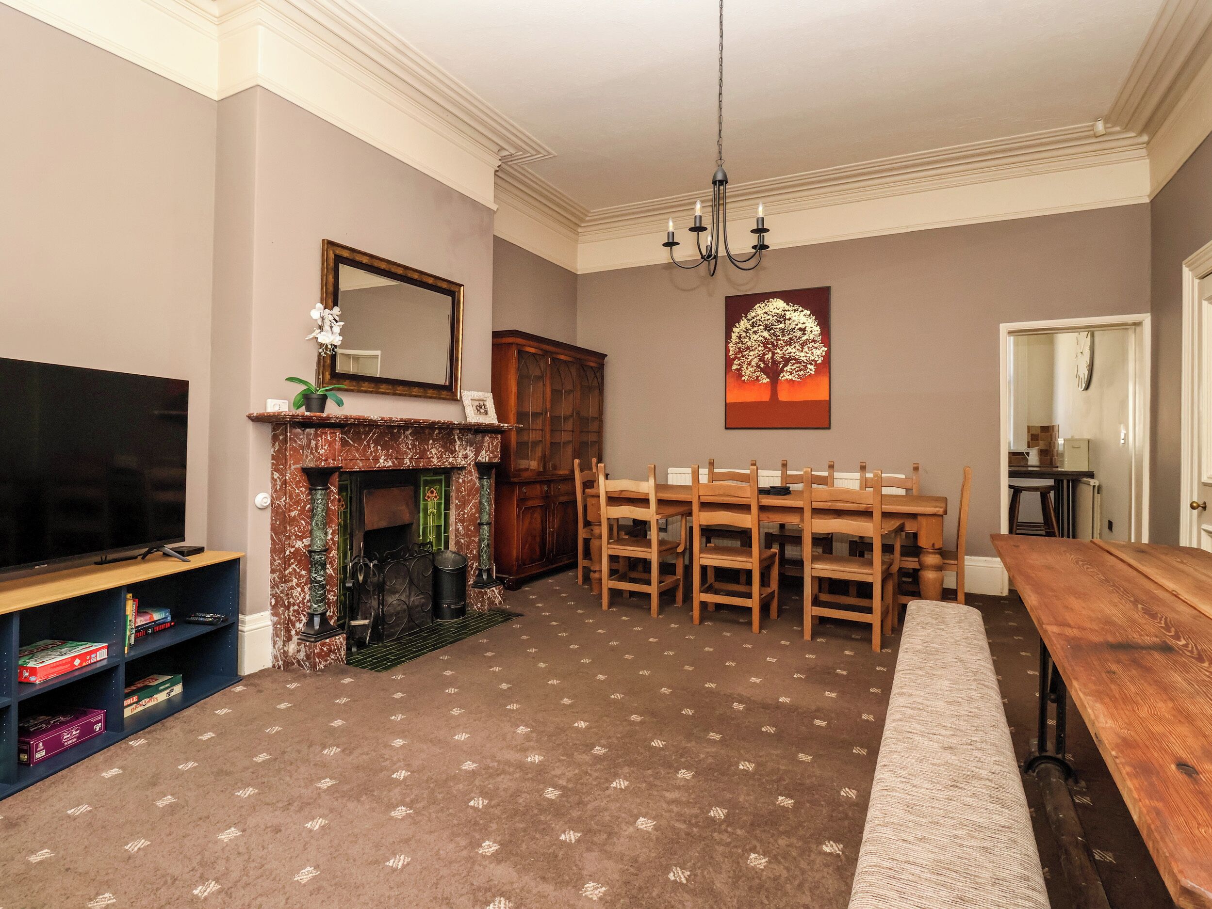 A living room with a fireplace, a television, a dining table with chairs, and a chandelier.