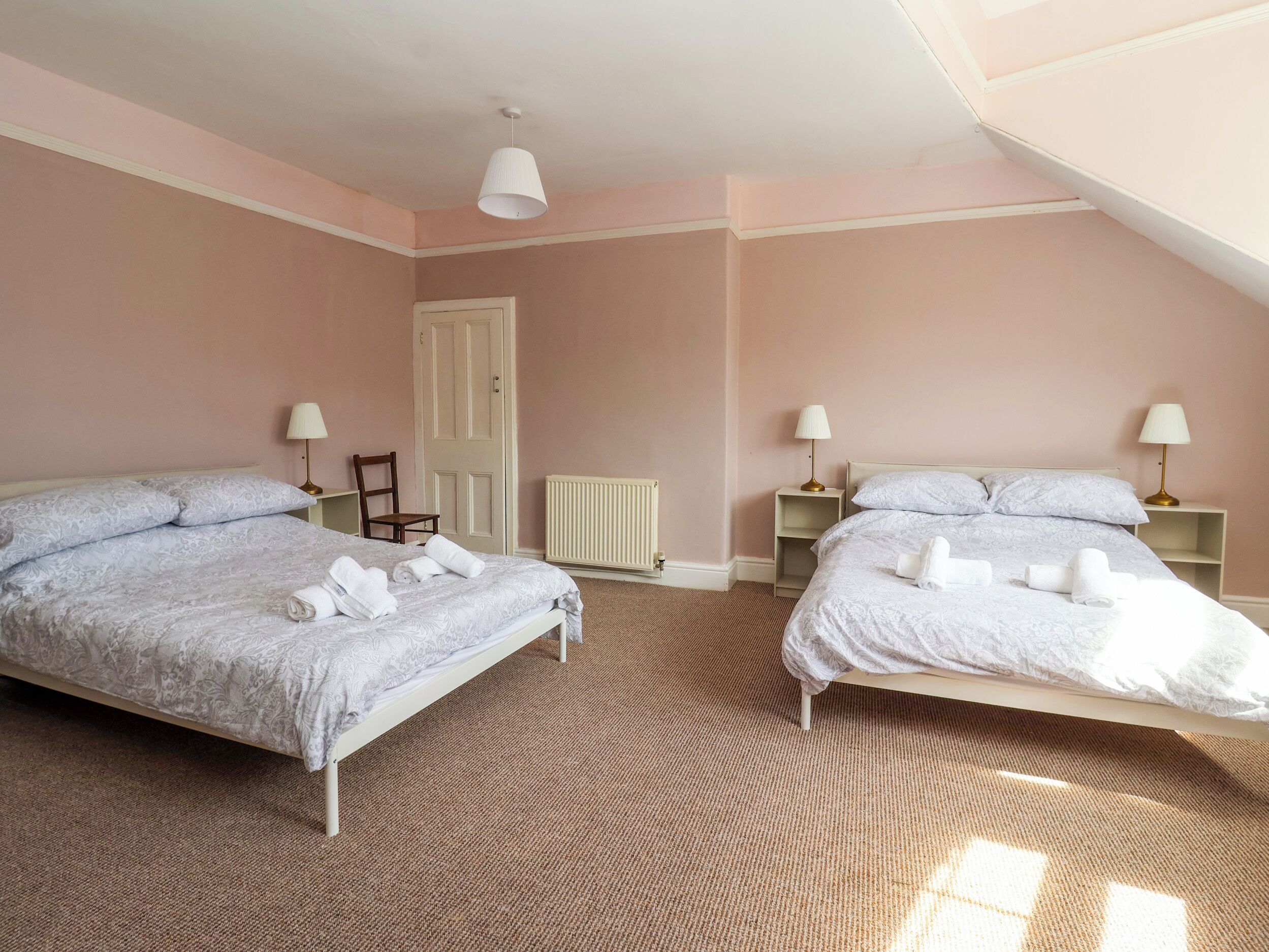 A bedroom with two beds, a radiator, a door, and two bedside tables with lamps.