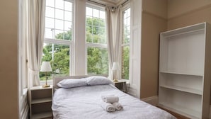 Une chambre à coucher comprenant un lit, deux tables de chevet, une armoire et de grandes fenêtres avec des rideaux.