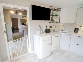 A compact kitchen with a white refrigerator, a flat-screen TV mounted above the counter, and a small sink.