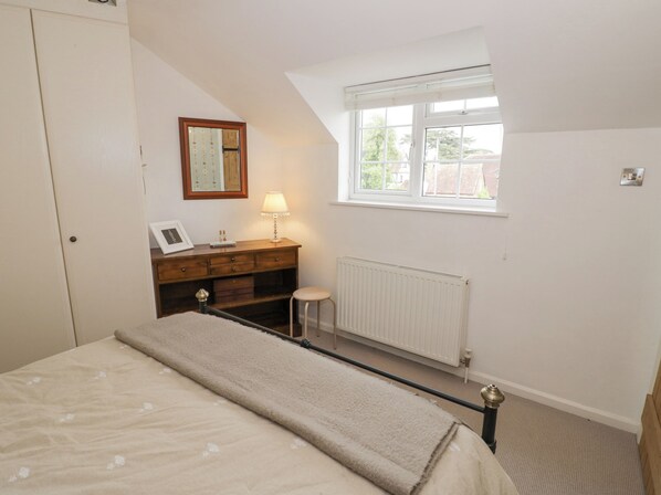 A bedroom with a bed, a dresser, a nightstand, a window, and a radiator.