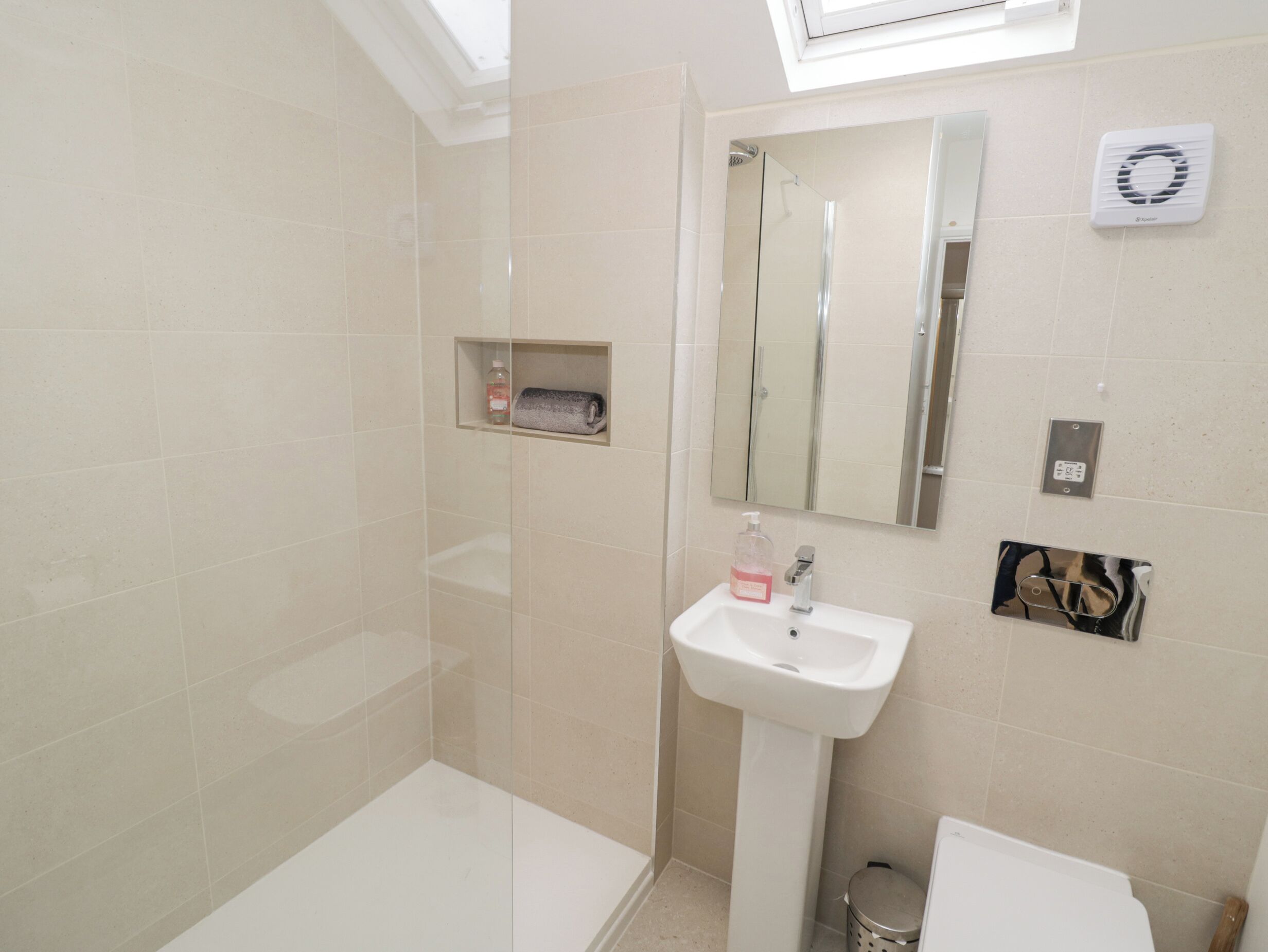 A modern bathroom with a glass shower enclosure, a pedestal sink, and a mirror above the sink.