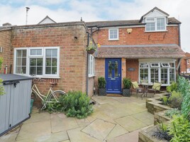 A brick cottage with a blue front door, a small patio with a table and chairs, and a bicycle parked outside.