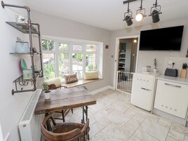 A kitchen with a dining area, white cabinets, a TV, and a window with a view of greenery.