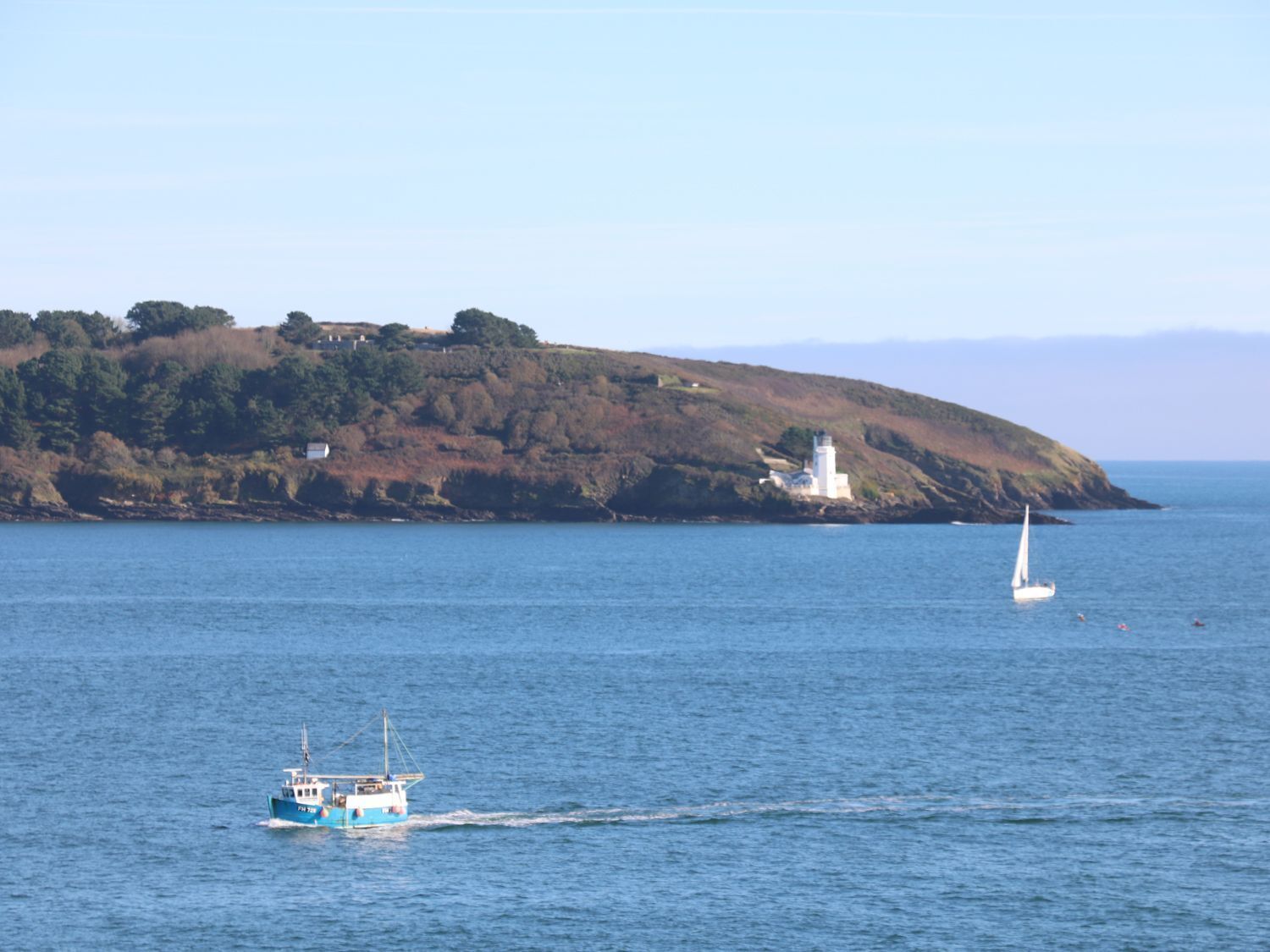 Escena costera con un faro, un velero y un barco pesquero en el agua.