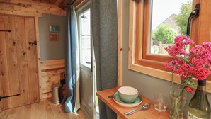 A wooden interior with a window, a table with a bowl, a wine bottle, and a vase with flowers. - Tower Hut (Ryde)