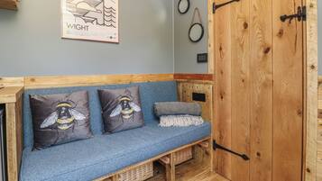 Un interior de madera con un sofá azul, tres almohadas con diseños de abejas, un cartel enmarcado y una puerta de madera con manija.