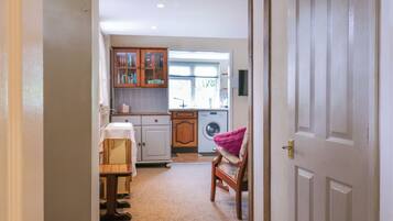 A narrow hallway leading to a kitchen with wooden cabinets, a washing machine, and a dining area with a table and chairs.