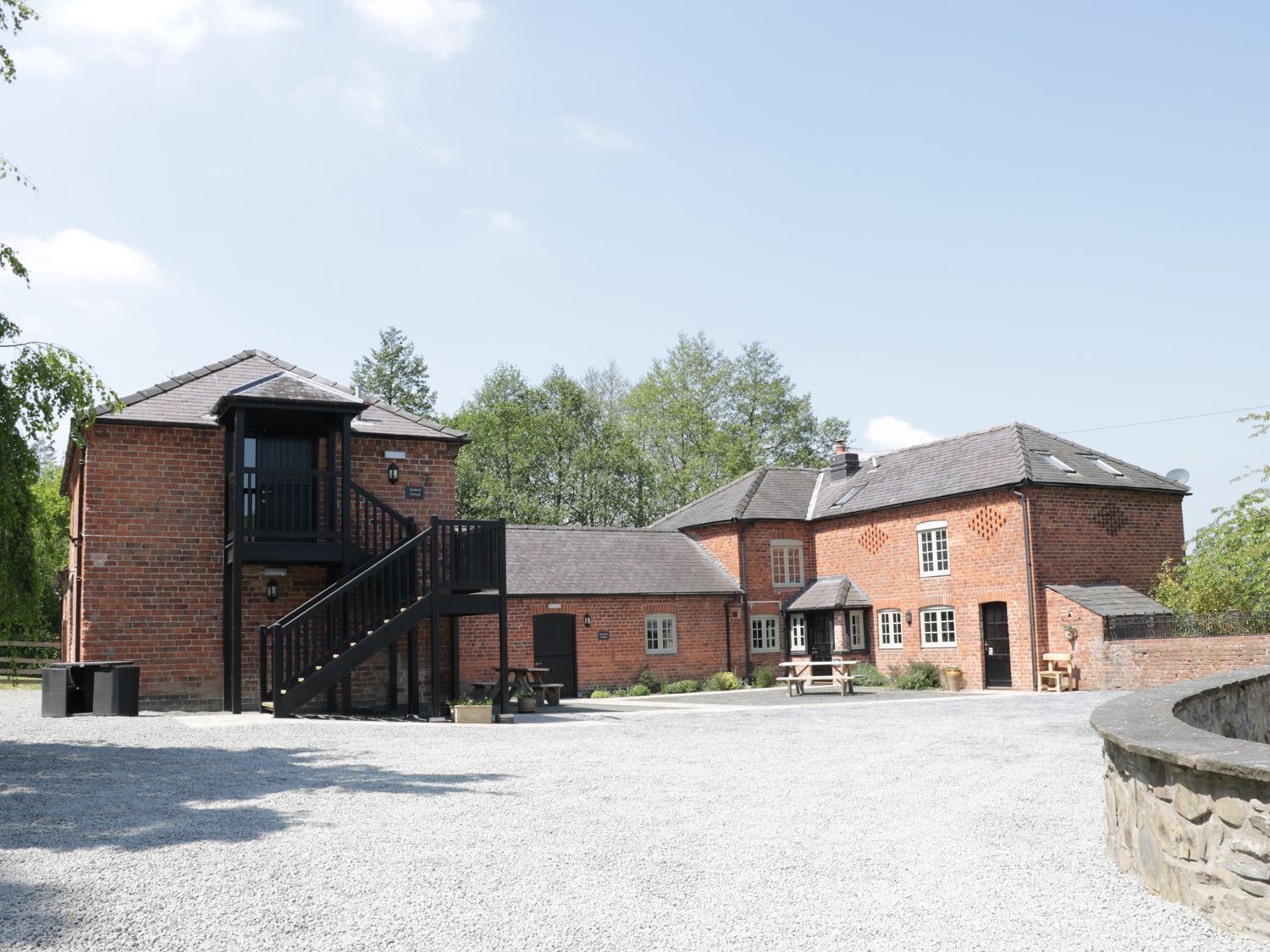 A brick building with a staircase leading to a balcony, a covered outdoor seating area, and a gravel courtyard.