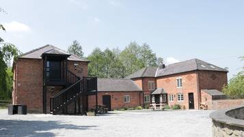A brick building with a staircase leading to a balcony, a covered outdoor seating area, and a gravel courtyard.