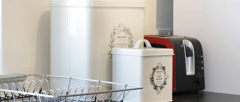 A kitchen counter with a metal drying rack, a white container with decorative text, and a black toaster.