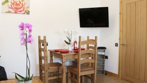 Et spiseområde med et træbord og stole, en vase med blomster og et fjernsyn ophængt på væggen.