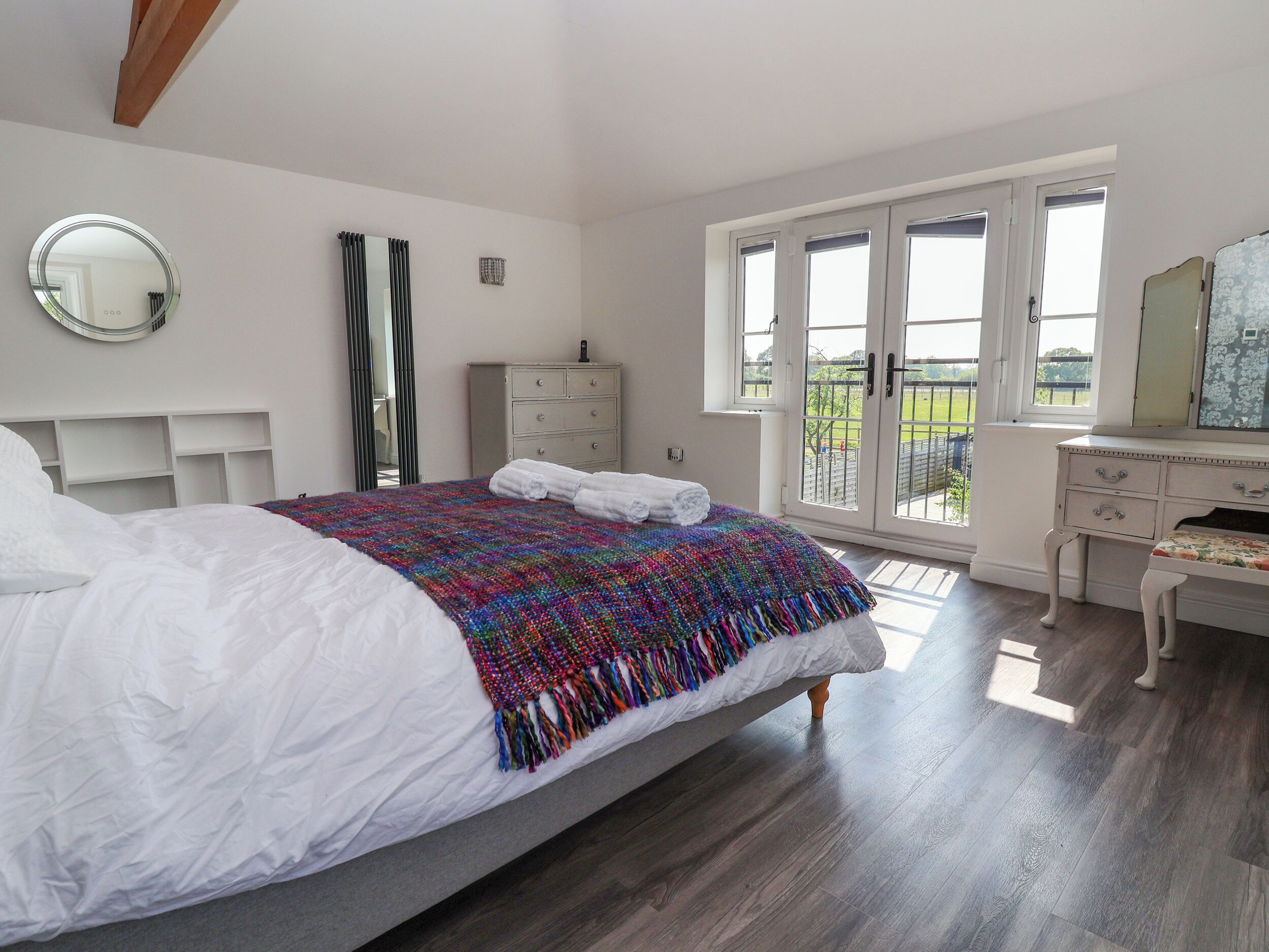 A bedroom with a bed, a dresser, a mirror, and a view of the outdoors through a door.