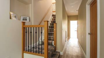 A staircase with wooden railings and a checkered carpet, leading to a door at the end of a hallway with wooden flooring.