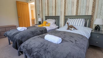 A room with two beds, each with a grey knitted blanket and a white towel. There are striped pillows and a stuffed octopus toy on one bed. The room has wooden paneling on the walls and a wooden door.