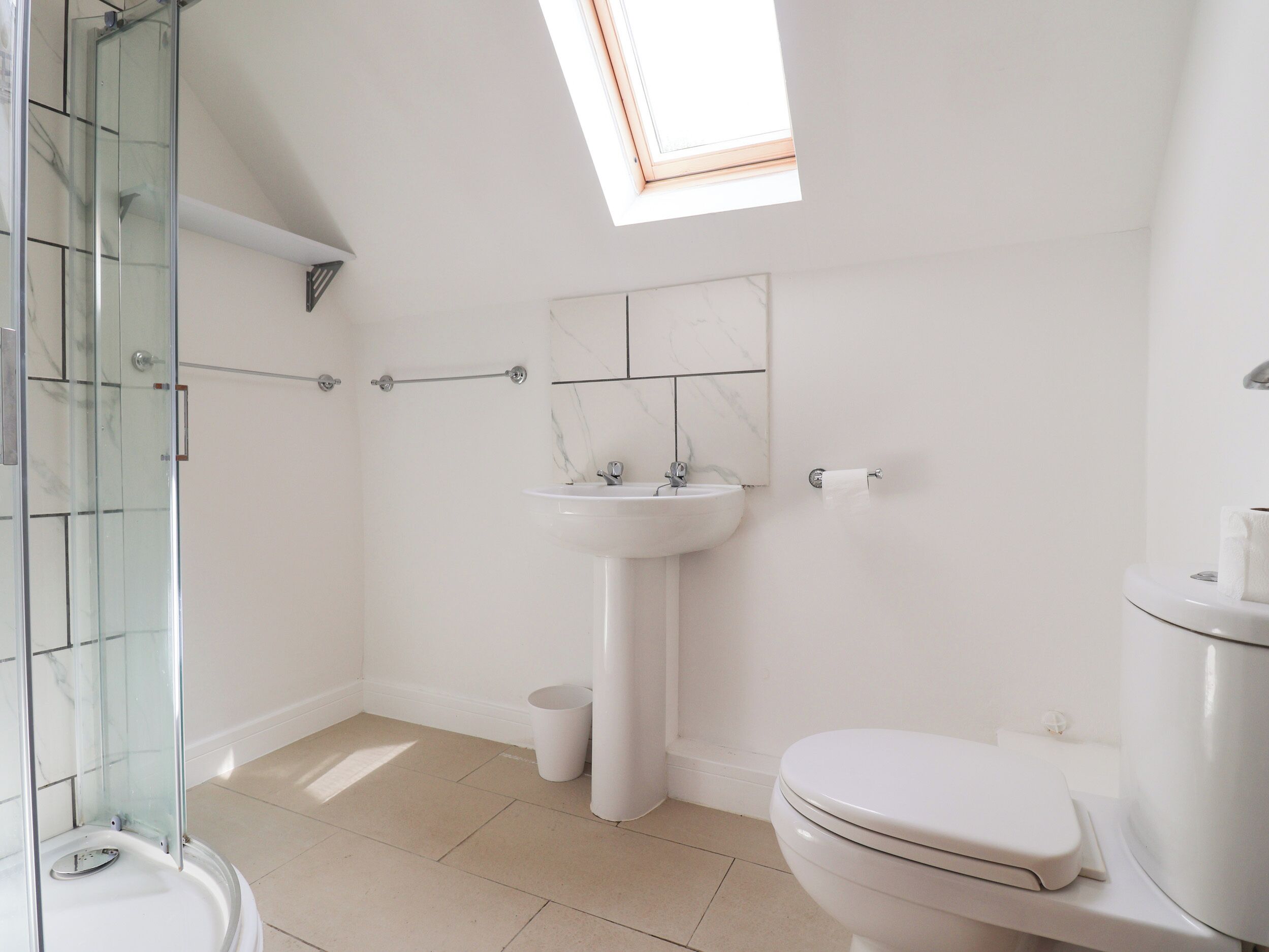 A modern bathroom with a glass shower enclosure, a pedestal sink, and a toilet.