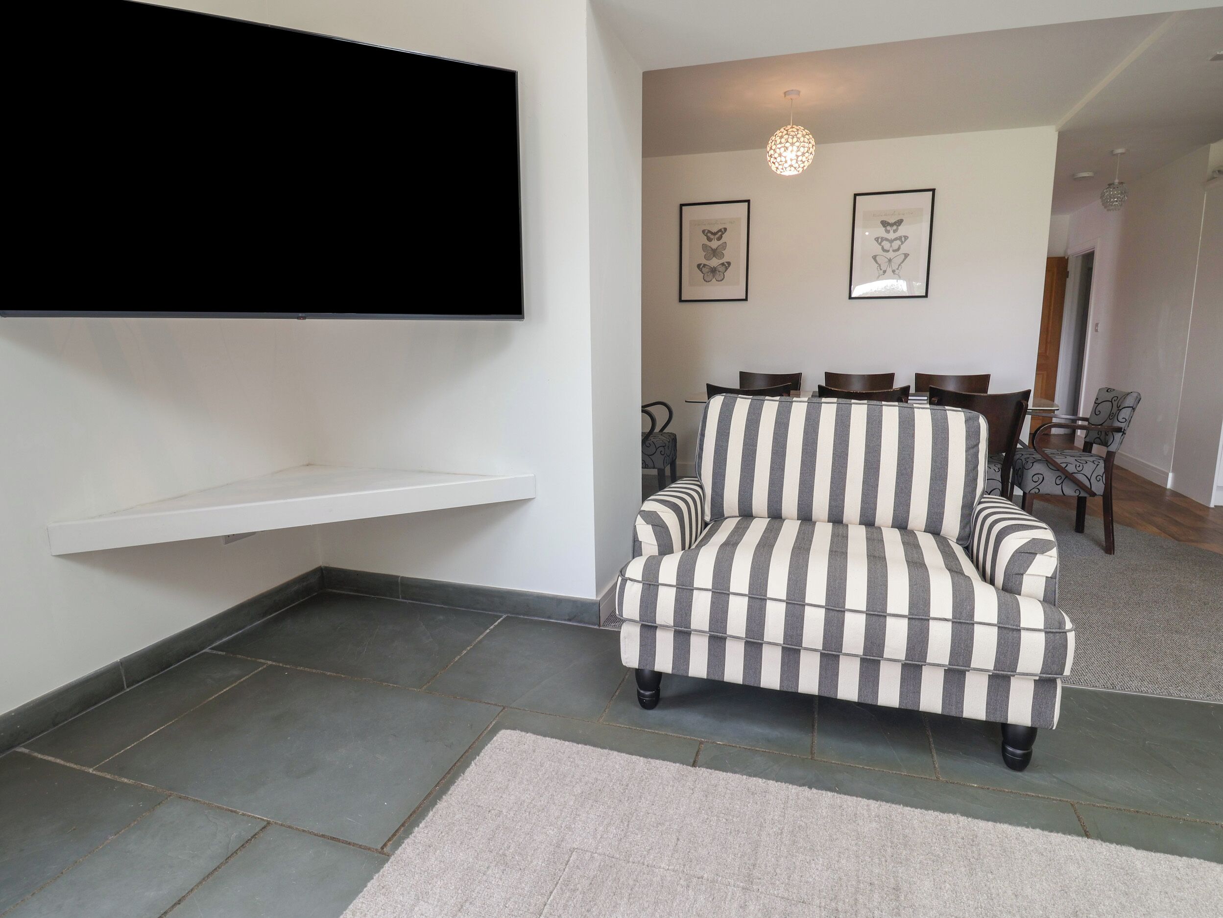 Een woonkamer met een gestreepte bank, een flatscreen televisie, vlinderkunst in lijsten en een eethoek met stoelen en een tafel.
