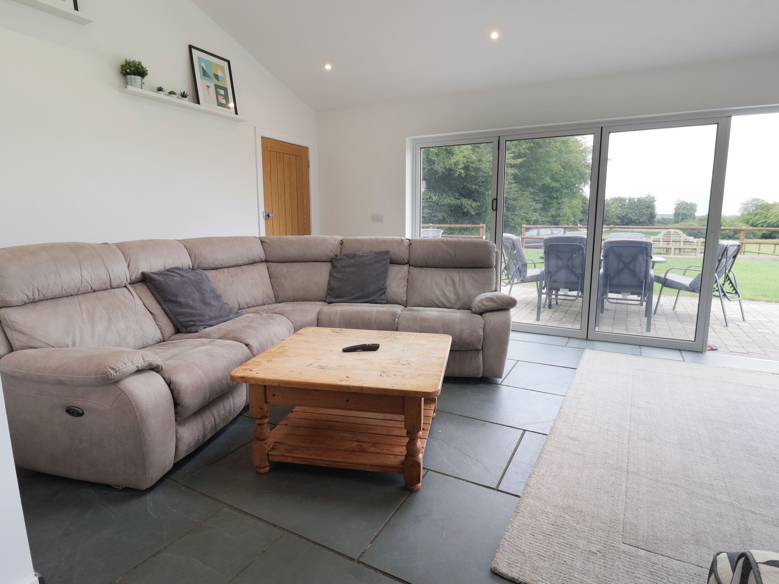 Una sala de estar moderna con un sofá seccional color beige, una mesa de centro de madera y un piso de vidrio corredizo que da a un patio exterior.