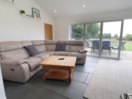 Una sala de estar moderna con un sofá seccional color beige, una mesa de centro de madera y un piso de vidrio corredizo que da a un patio exterior.