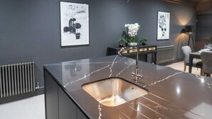 A modern kitchen with a marble countertop, a sink, and a pendant light. There are framed pictures on the wall and a radiator below. - Tower View (Scarborough)