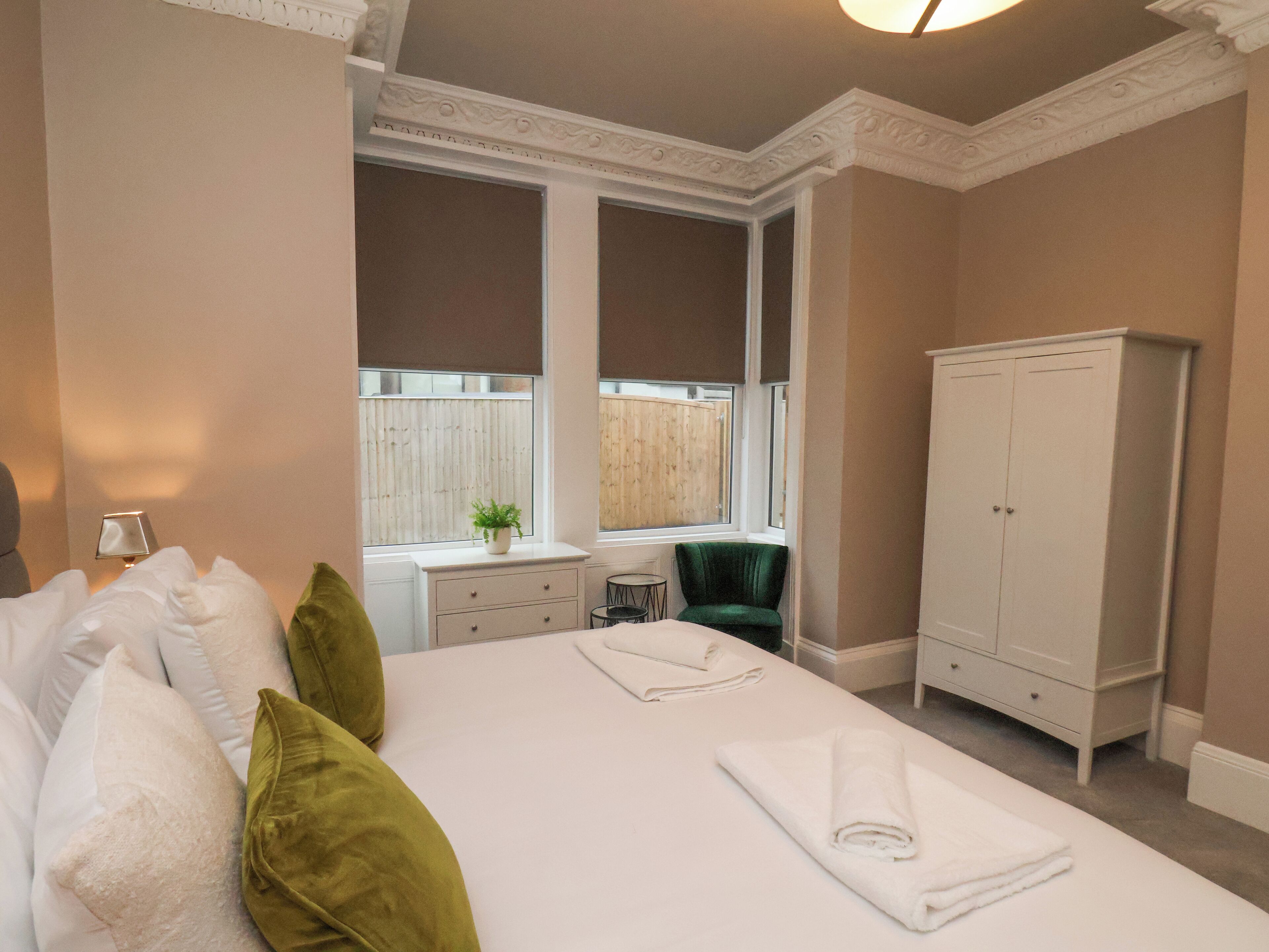 A hotel room with a large bed, a desk, a chair, and a wardrobe.