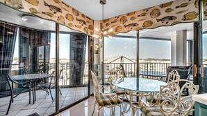 Un comedor con mesa y sillas de vidrio, techo con diseño y vista de la ciudad a través de amplias ventanas.