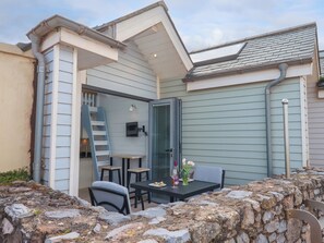 A patio with a stone wall, a table with chairs, and a small staircase leading to an upper level. - Beach Hut 5 (Teignmouth)
