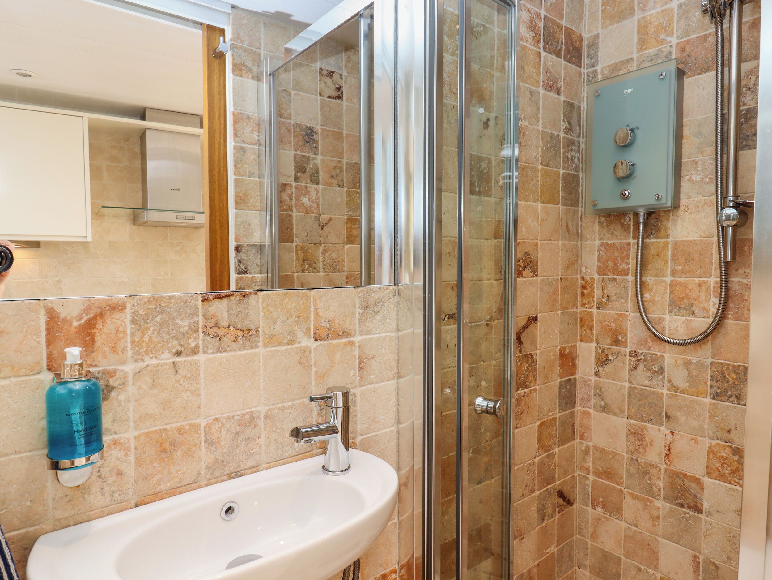 Un baño con ducha de mampara de vidrio, un lavamanos blanco y dispensador de jabón.