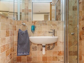 A bathroom with a white sink, a glass shower enclosure, and a towel hanging on a rack. - Beach Hut 5 (Teignmouth)