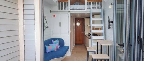 A compact, modern interior with a loft bedroom, a small kitchenette, and a seating area with a sofa and stools.