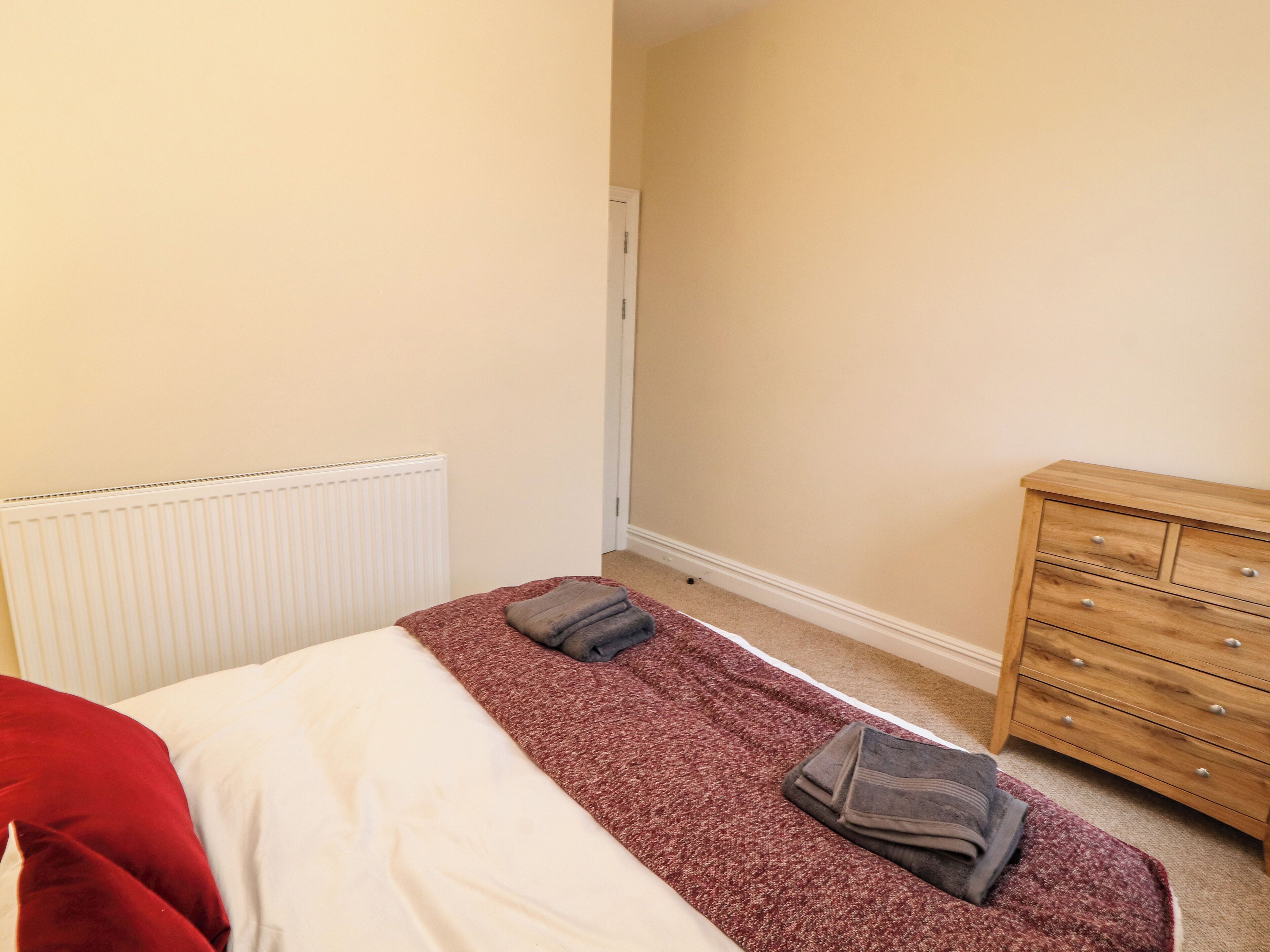 Ein Schlafzimmer mit Bett, Heizkörper, Holzkommode und Tür.