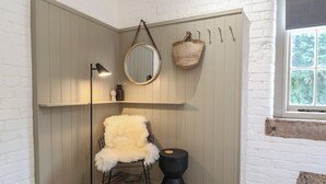 A corner room with a white brick wall, a round mirror, a fluffy chair, a black stool, and a hanging basket. - Beech Cottage - Fold Yards (Matlock)
