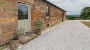 A stone building with a gravel driveway, a door, and two potted plants. - Beech Cottage - Fold Yards (Matlock)