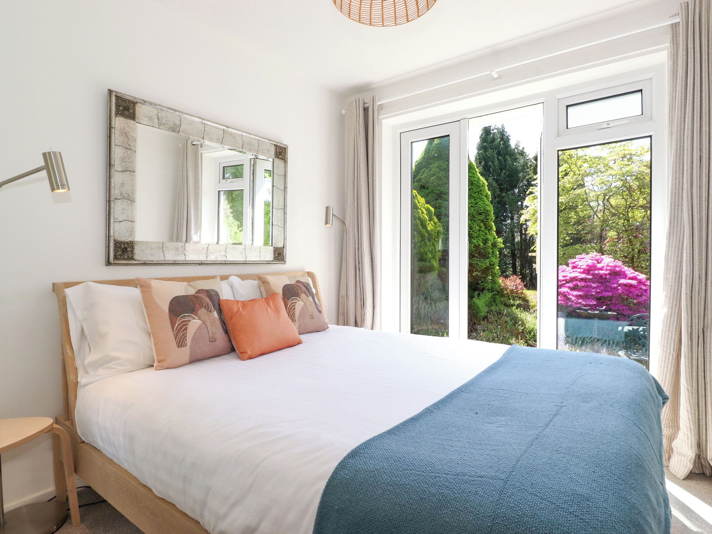 Un dormitorio con una cama grande, un espejo y vistas al verde exterior.