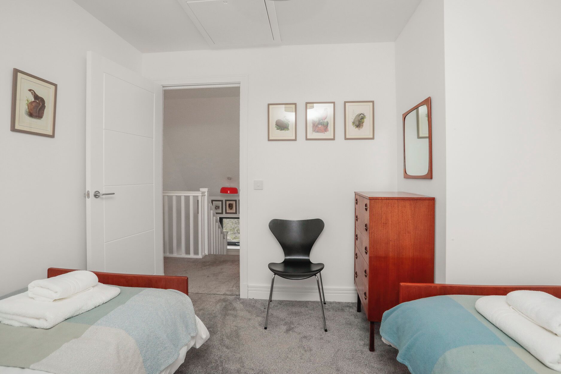 A bedroom with two single beds, a wooden dresser, a black chair, and a door leading to another room.