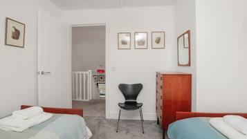 A bedroom with two single beds, a wooden dresser, a black chair, and a door leading to another room.