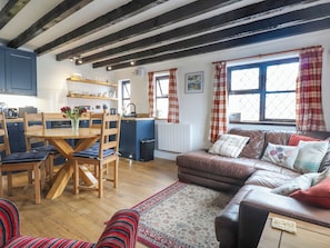 A cozy living room with a brown leather sofa, a wooden dining table with chairs, and a patterned rug. - The Studio Cottage (Cemaes Bay)