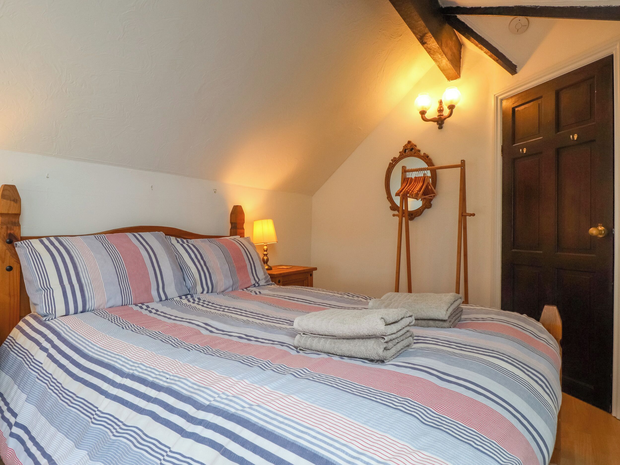 A bedroom with a large bed, a wooden headboard, a bedside lamp, a mirror, and a wooden door.