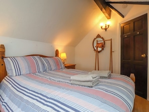 A bedroom with a large bed, a wooden headboard, a bedside lamp, a mirror, and a wooden door. - The Studio Cottage (Cemaes Bay)