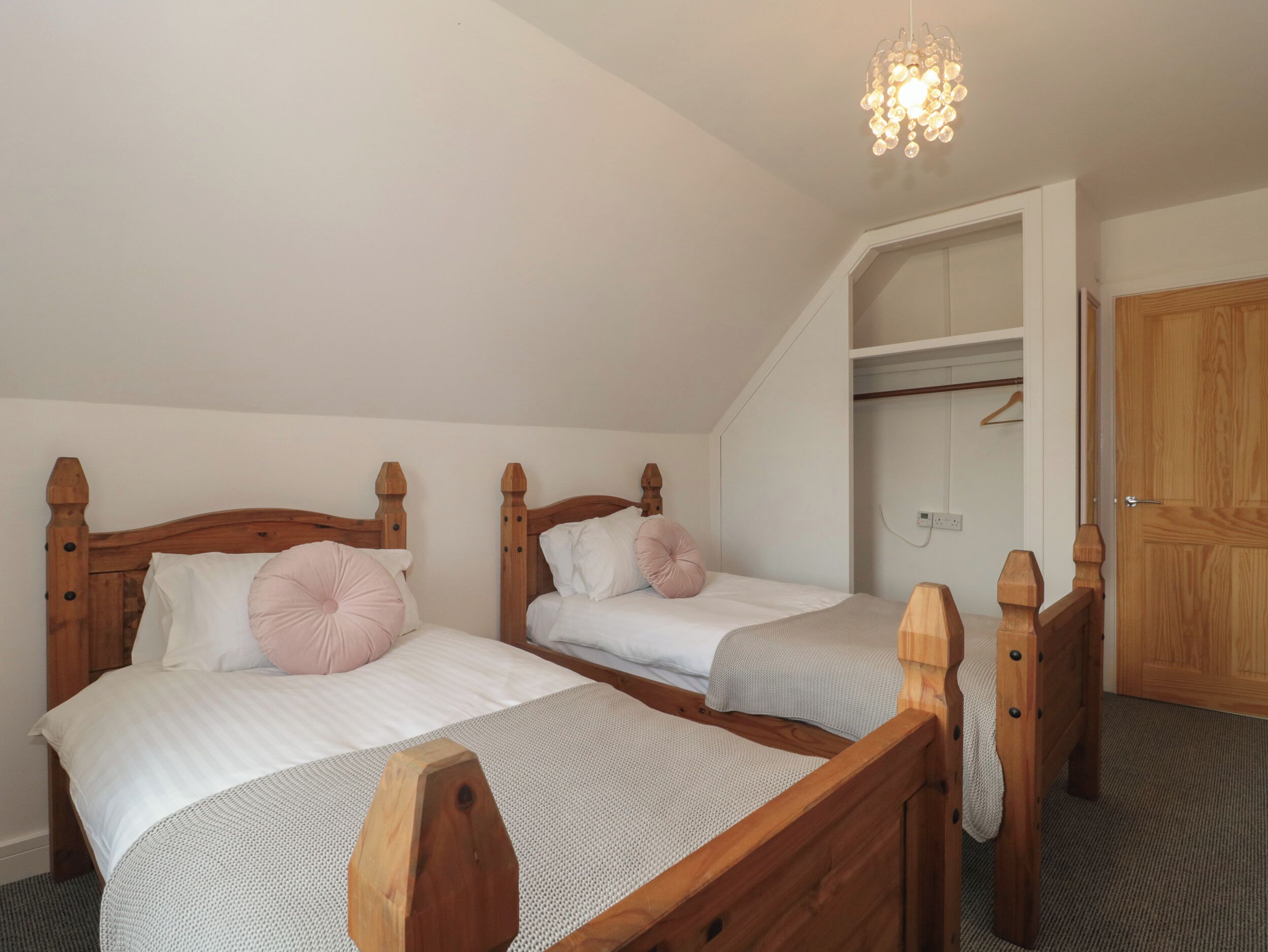 Un dormitorio con dos camas de madera, una lámpara colgante y un armario con espejo.