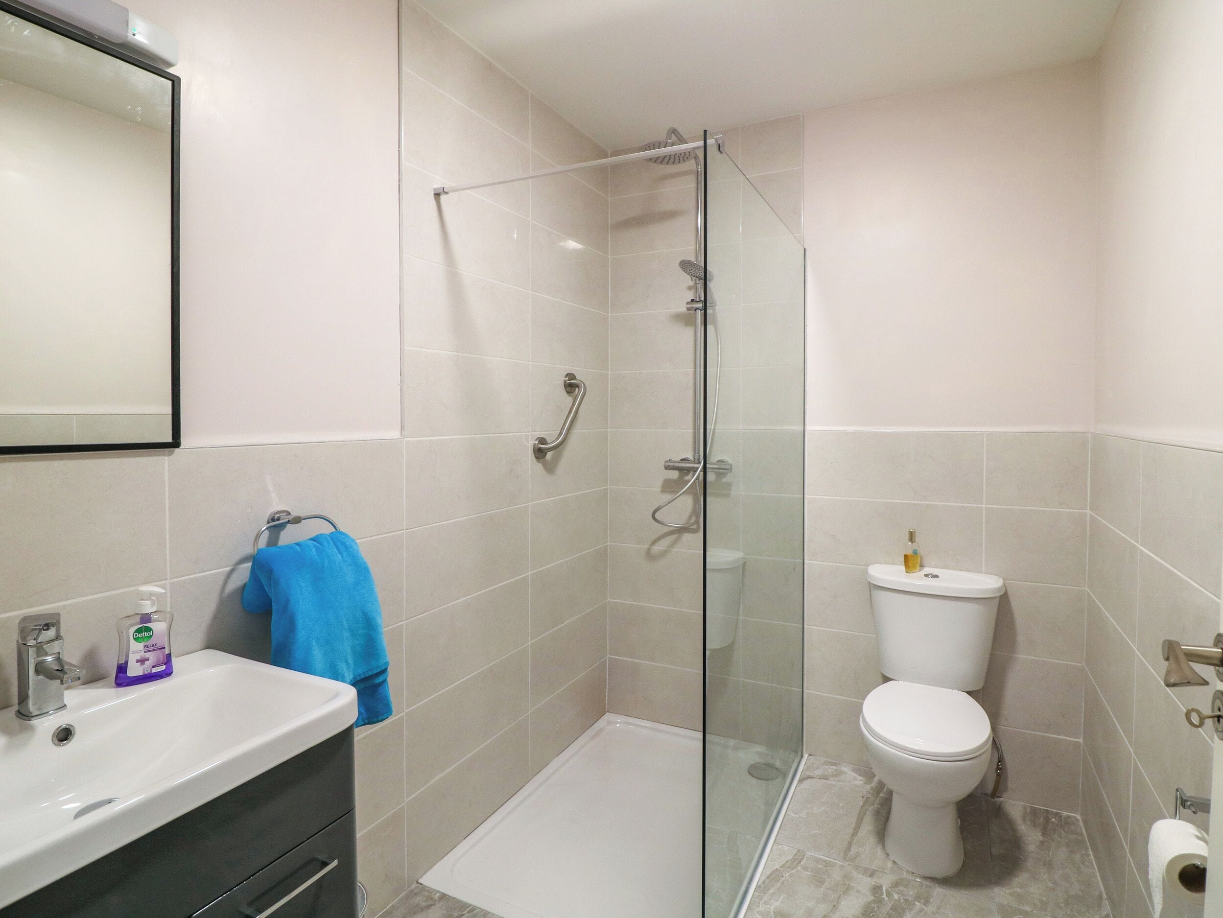 A modern bathroom with a glass-enclosed shower, a white toilet, and a sink with a soap dispenser.