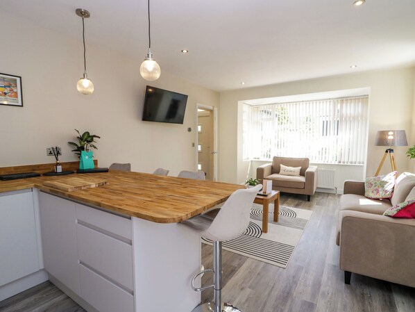 A modern kitchen with a wooden island, a dining area with a sofa, and a TV mounted on the wall. - Brynmar (Morecambe)