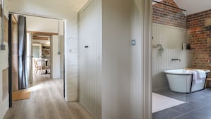 Un intérieur moderne avec un plancher en bois, une porte blanche et une salle de bain dotée d’une baignoire et d’un sol carrelé.