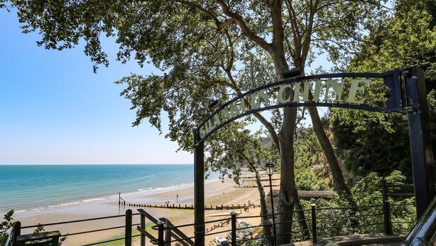 Una platja amb una escala de fusta que baixa fins a la riba, un cartell que diu 'SANDY HILL' i un cubell d'escombraries amb la inscripció 'LITTER'.