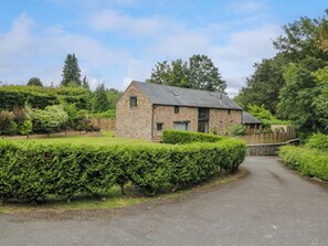 A stone house with a paved driveway, surrounded by well-maintained hedges and trees. - The Ivy Barn (Abergavenny)